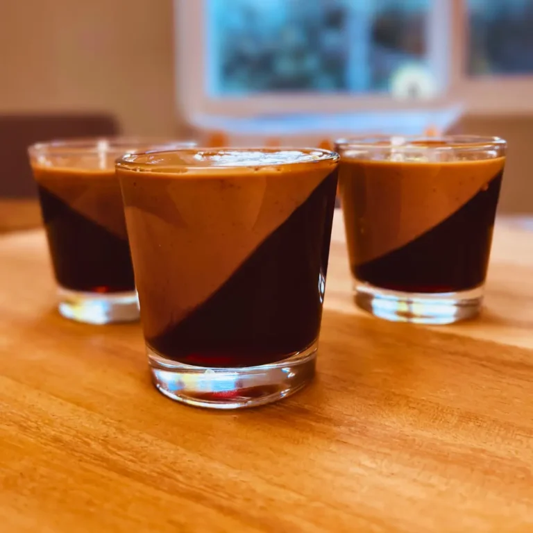 Three glass cups containing two-toned coffee jelly dessert with diagonal layers - dark coffee jelly on bottom and lighter latte-colored jelly on top, arranged on a wooden table"
