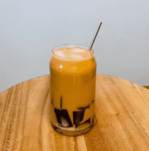 Glass of iced yuenyeung (coffee-milk tea) drink with dark jelly stripes along the sides, served with a metal straw on a wooden table
